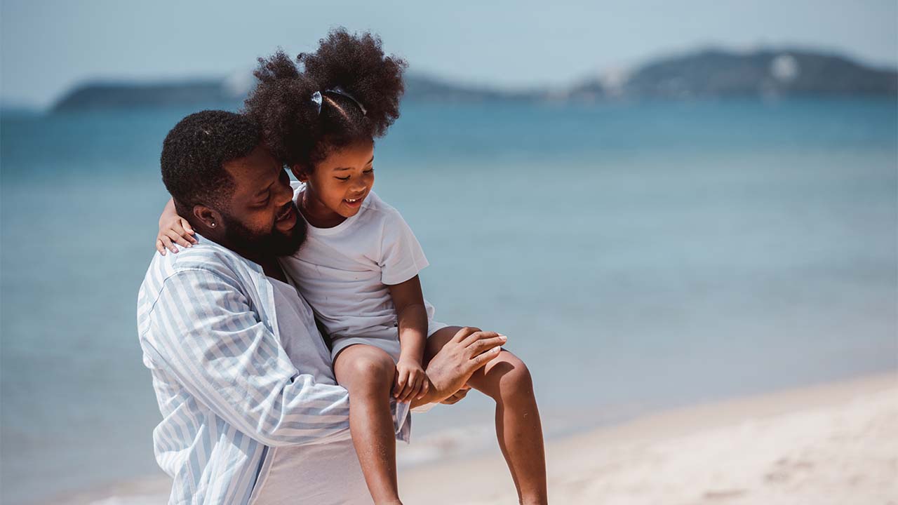 pai brinca com sua filha na praia, representando o sonho de constituir uma família